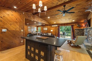 A wooden cabin interior with a central bar, a stone fireplace, and a ceiling fan. - Private Lake | 50 acres | Secluded Cabin | Hiking (Hawley)