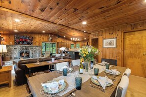 A wooden-paneled room with a fireplace, a dining table set for six, and a television mounted on the wall. - Private Lake | 50 acres | Secluded Cabin | Hiking (Hawley)