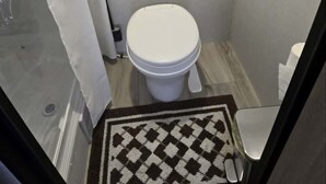 Pieni, erillinen kylpyhuone, jossa on wc, suihkutila ja kuviollinen matto lattialla.