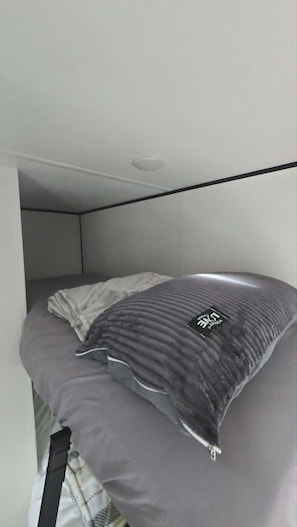 A compact bed with a grey pillow and a tag, in a room with a white ceiling and walls. - Cozy Camper Getaway | Sleeps 4 | WiFi (Auburn)