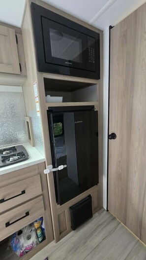 A compact kitchenette with a microwave, refrigerator, and a small stove.