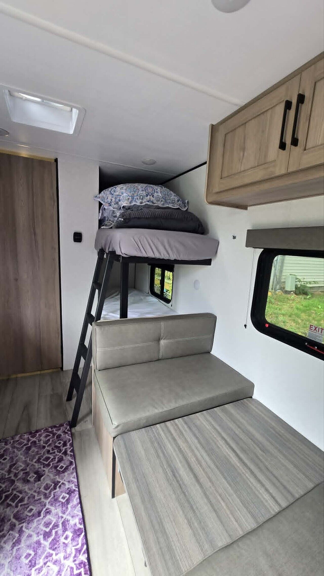 Ein kompaktes Wohnmobil-Interieur mit Etagenbett, einer kleinen Küchenzeile und einem Fenster mit Blick ins Freie.