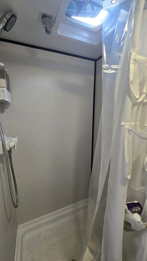A shower with a showerhead, a handheld shower, and a curtain. - Cozy Camper Getaway | Sleeps 4 | WiFi (Auburn)