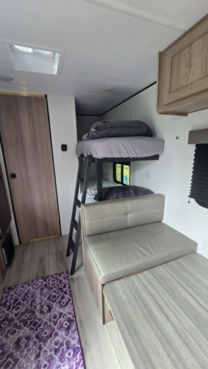 Ein kompaktes Wohnmobil-Interieur mit Schlafgeschoß, einer kleinen Sitzecke und einer Tür zu einem Außenbereich.
