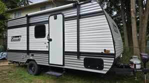 A Coleman RV parked in a grassy area with trees in the background. - Cozy Camper Getaway | Sleeps 4 | WiFi (Auburn)