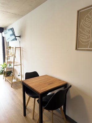 A room with a wooden table, two black chairs, a wall-mounted TV, and a framed leaf artwork.