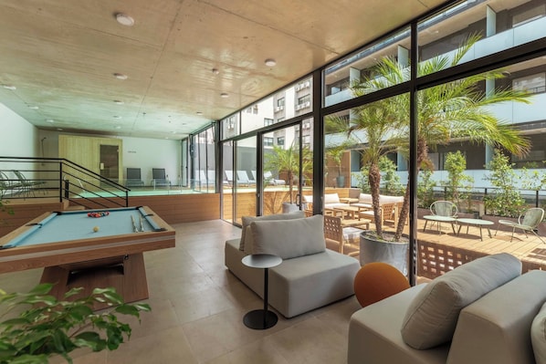 A modern indoor space with a pool table, seating area, and large windows overlooking a courtyard.