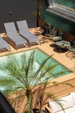A pool area with lounge chairs and a small table, surrounded by potted plants. - Modern WTC Studio Apartment | Gym + Pool (Montevideo)