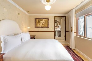 A hotel room with a large bed, a nightstand, a wall-mounted lamp, a framed picture, and a view of the bathroom through an open door. - Royva Bo-Kaap (Cape Town)