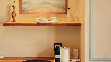A room with a wooden desk, a chair, a framed painting, a vase with flowers, and a water bottle.