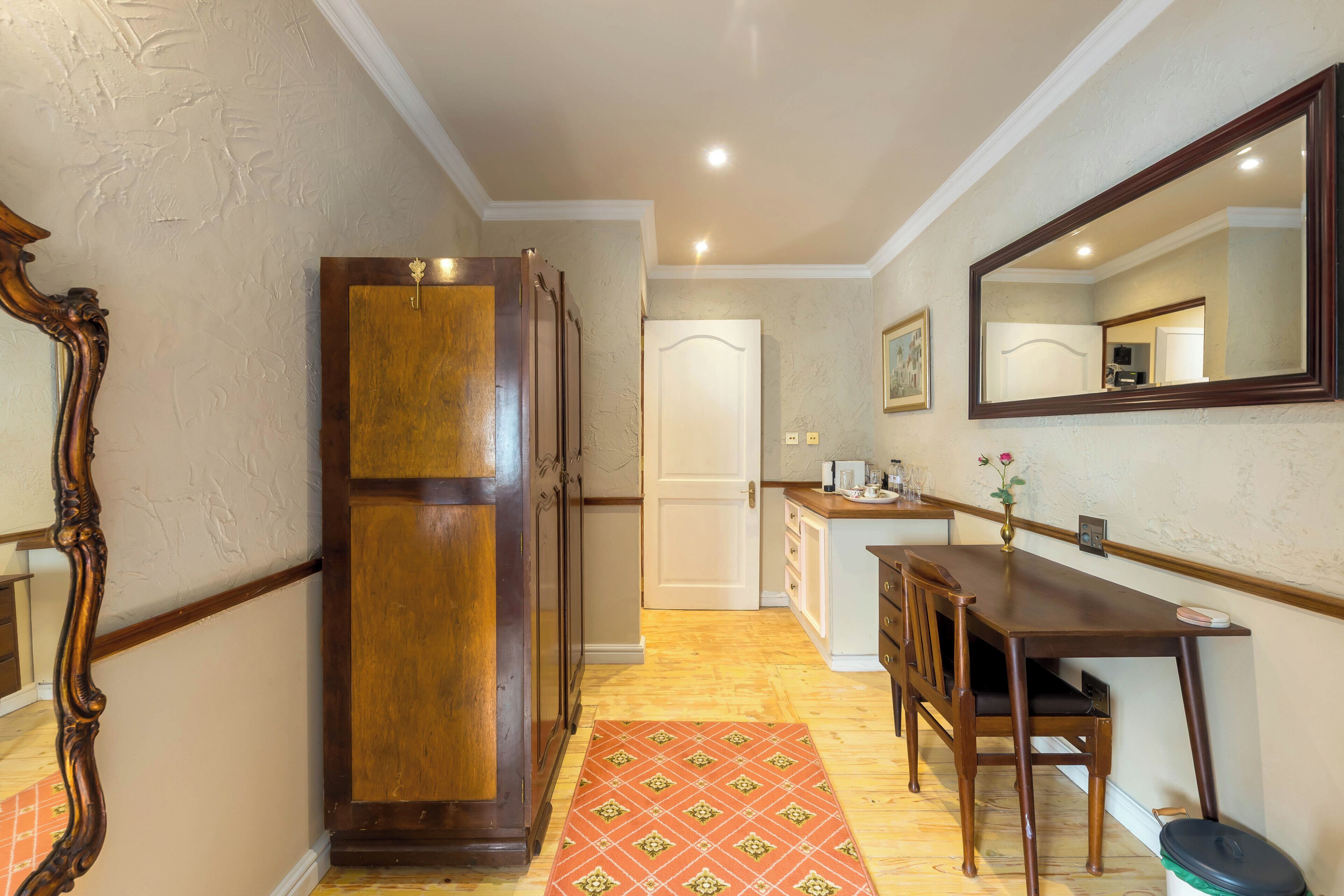A hallway with a wooden cabinet, a dining table with chairs, a mirror, and a door.
