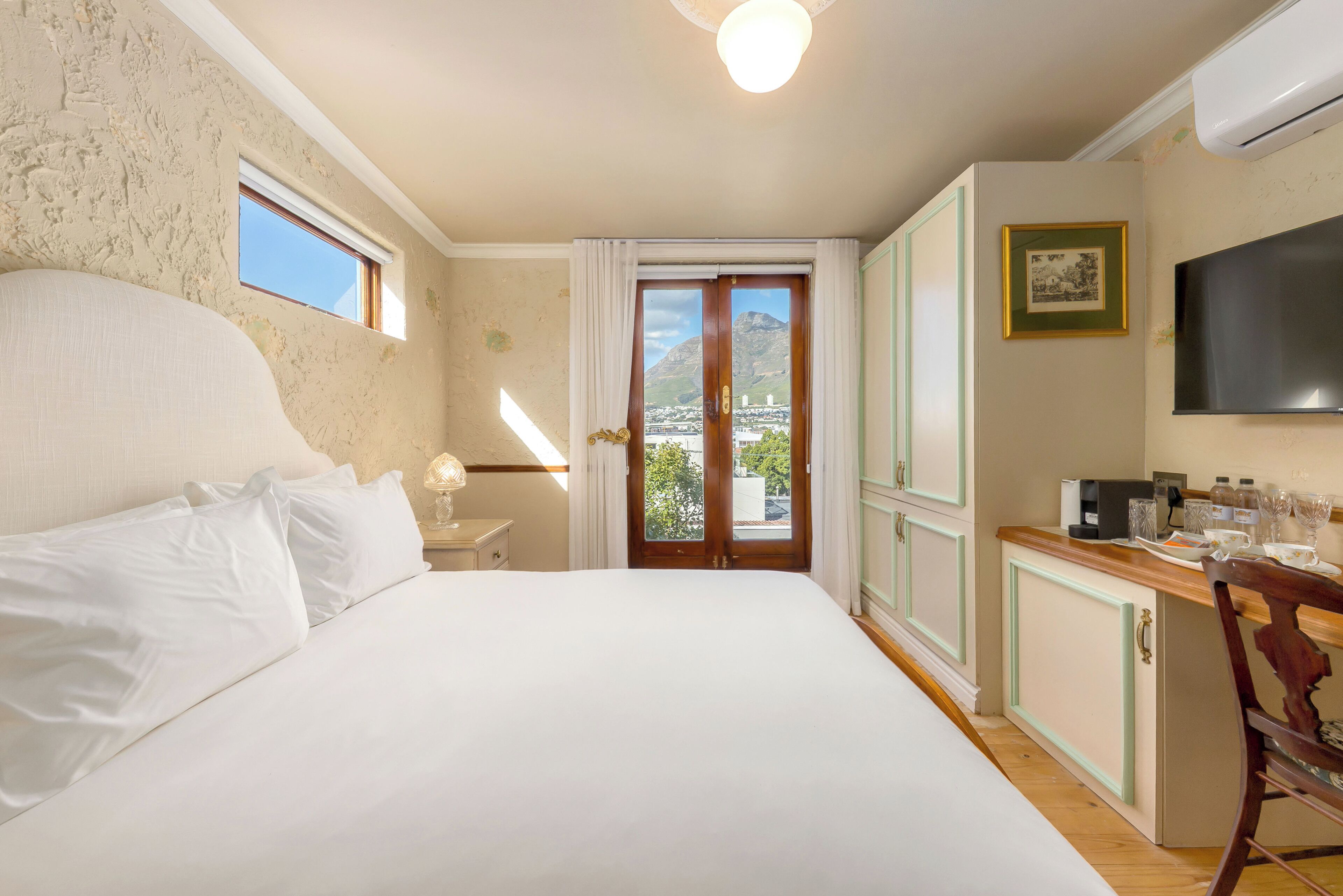 Un dormitorio con una cama grande, un escritorio con televisor de pantalla plana y vista a la montaña desde una puerta.