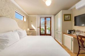 A bedroom with a large bed, a desk with a flat-screen TV, and a view of a mountain through a door. - Royva Bo-Kaap (Cape Town)