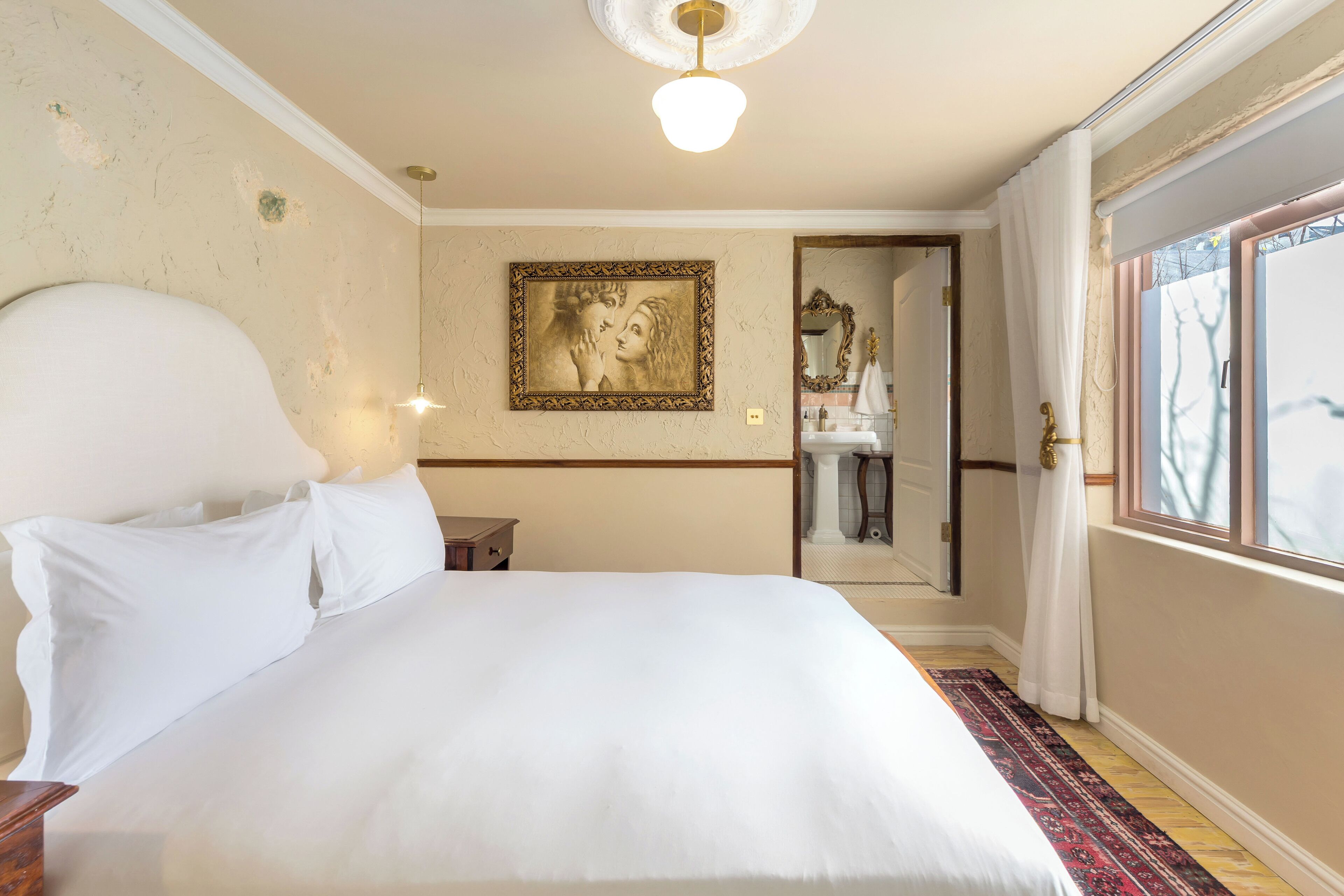 A hotel room with a large bed, a nightstand, a wall-mounted lamp, a framed picture, and a bathroom visible through an open door.