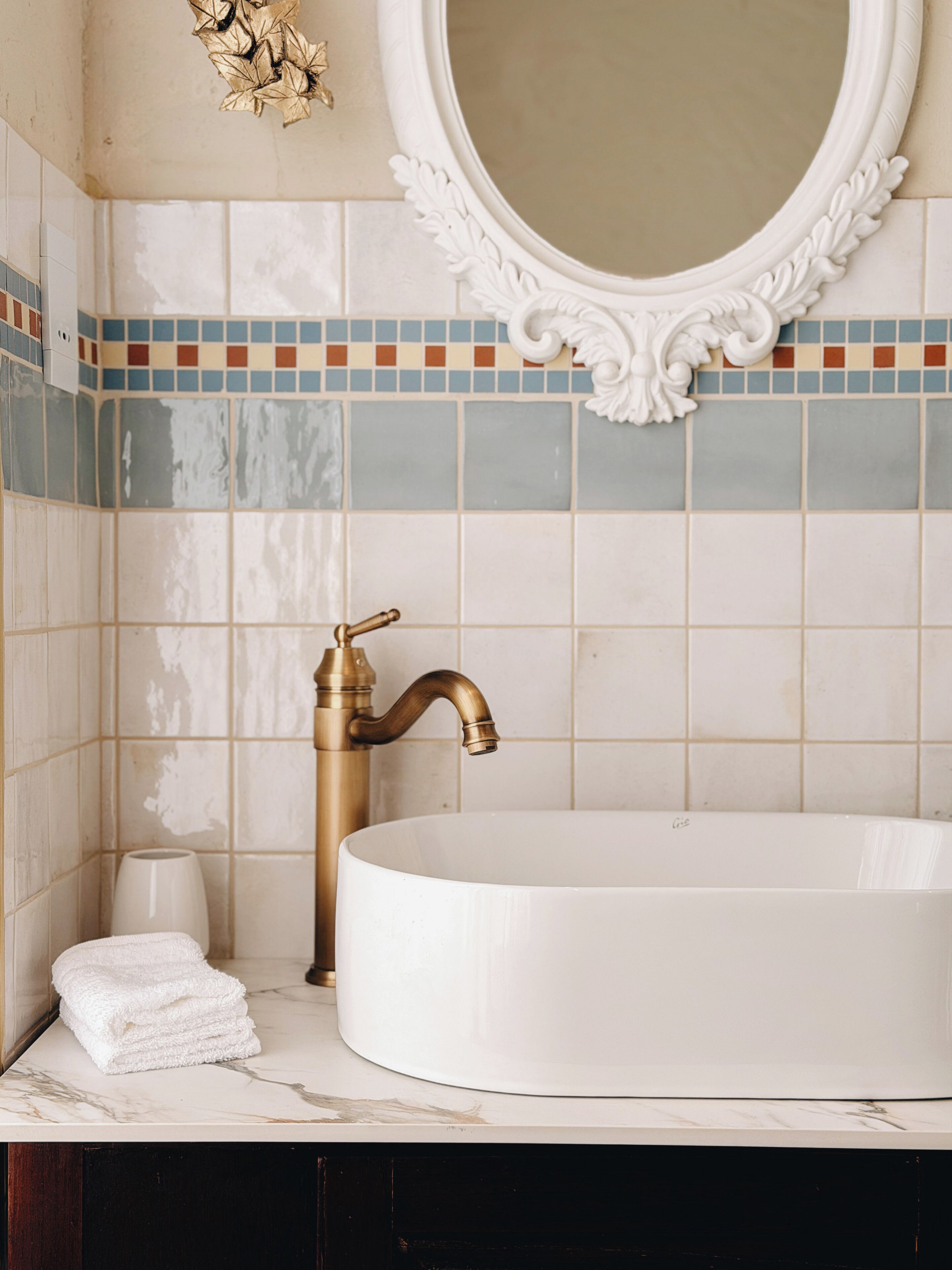 A bathroom with a white sink, gold faucet, and a mirror with an ornate frame.