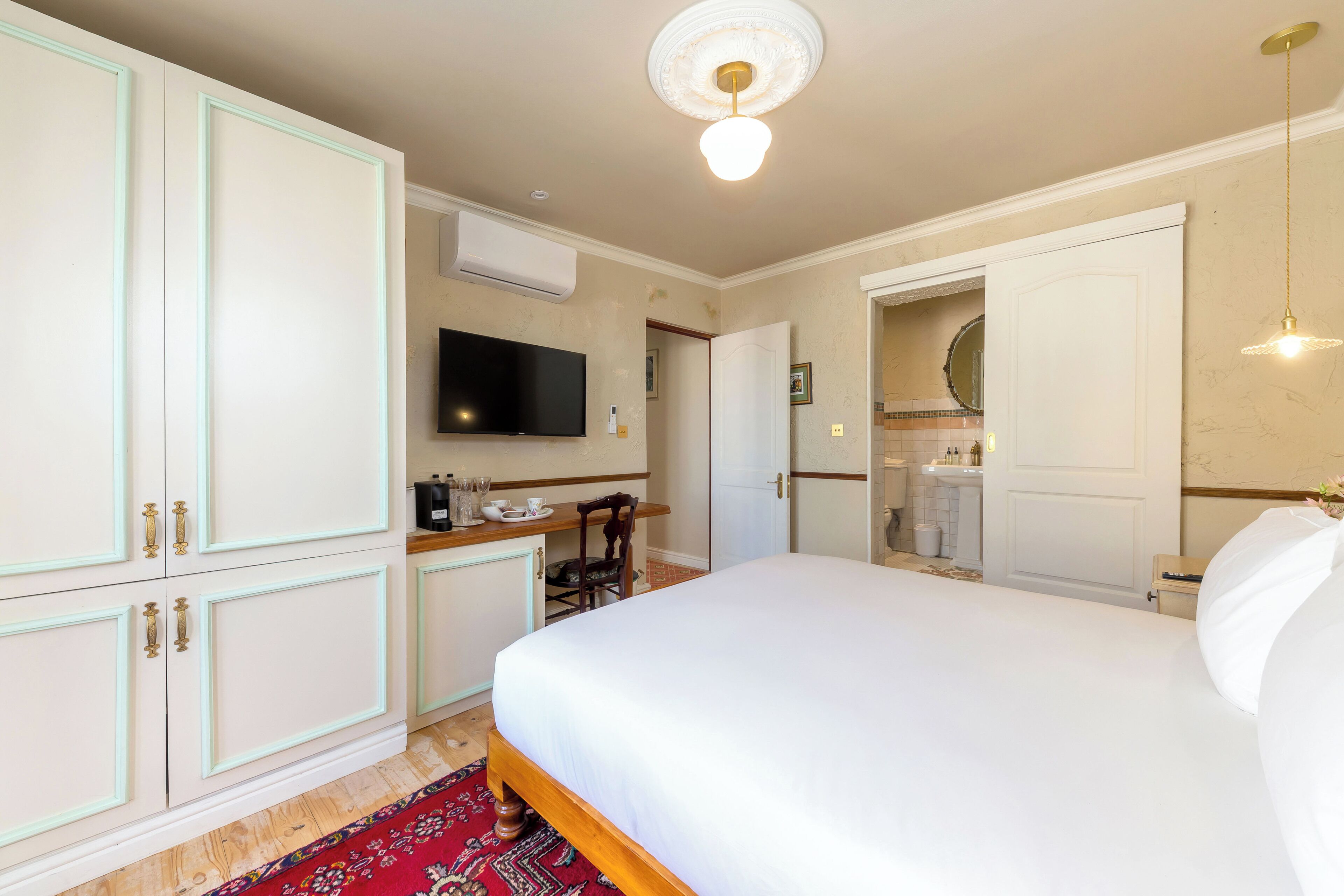A bedroom with a bed, wardrobe, television, and a bathroom visible through an open door.