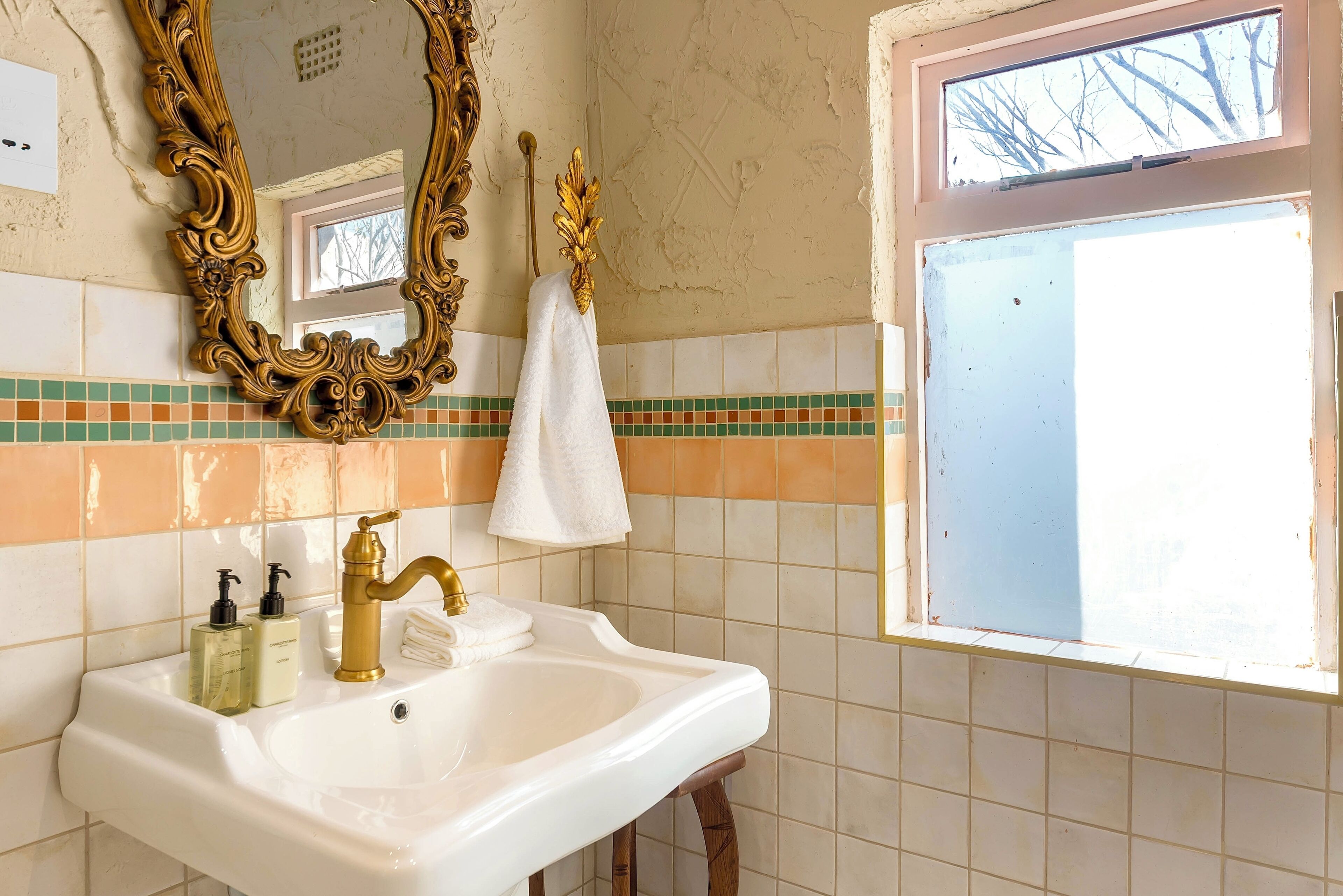 A bathroom with a white sink, gold faucets, and a large ornate mirror.