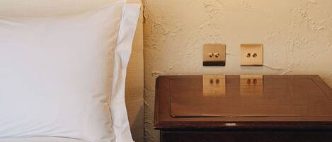 A bed with white bedding, a wooden nightstand with two light switches, and a hanging light fixture.