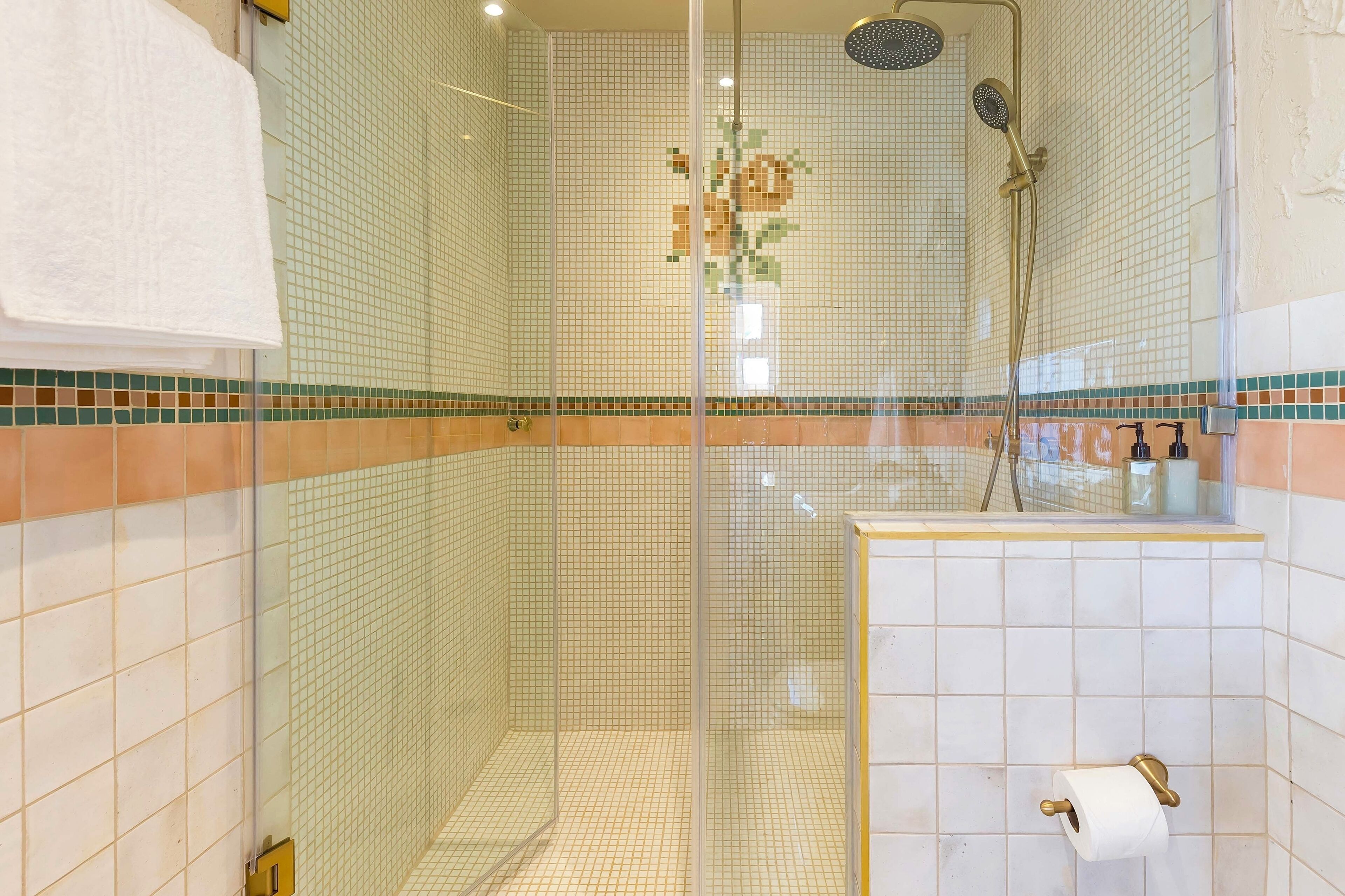 A glass-enclosed shower with a handheld showerhead and a wall-mounted showerhead.