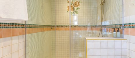 A glass-enclosed shower with a handheld showerhead and a wall-mounted showerhead.