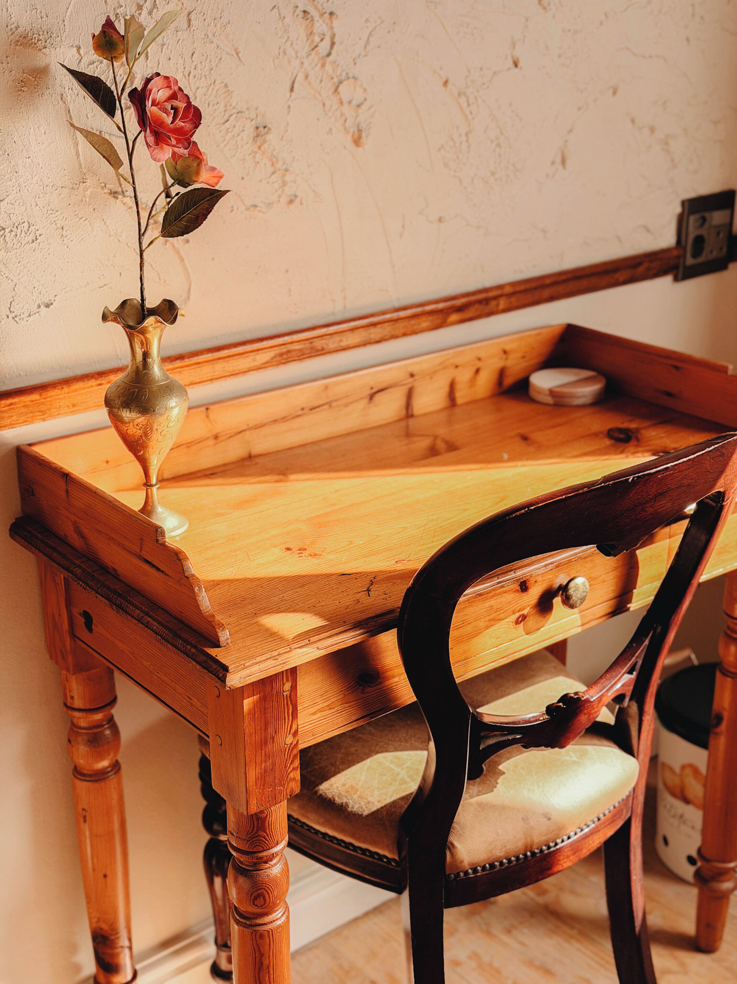 Ein Holztisch mit Blumen in einer Vase, ein Stuhl mit Kissen und eine hölzerne Bank.