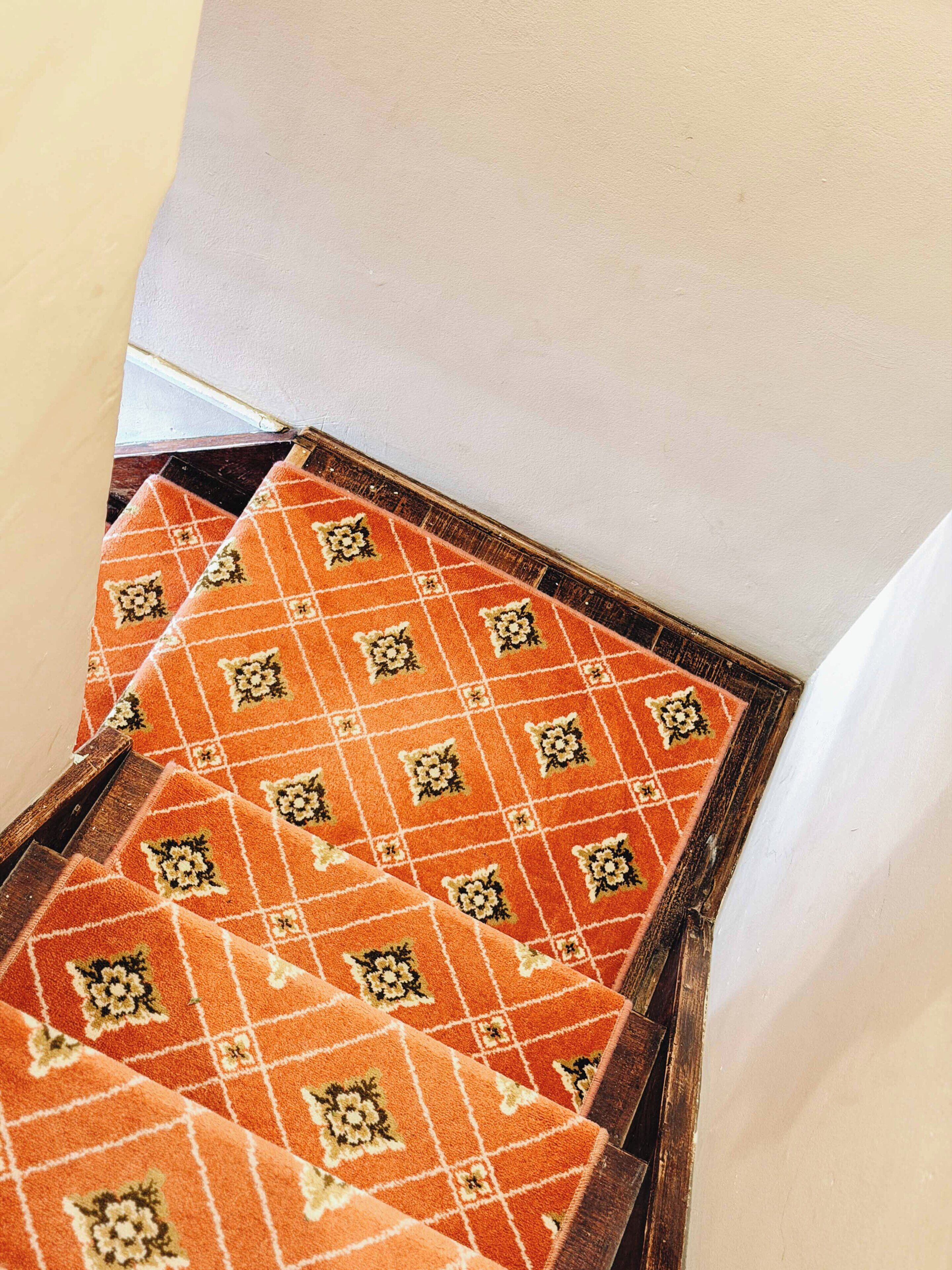 A staircase with orange patterned carpets and wooden handrails.