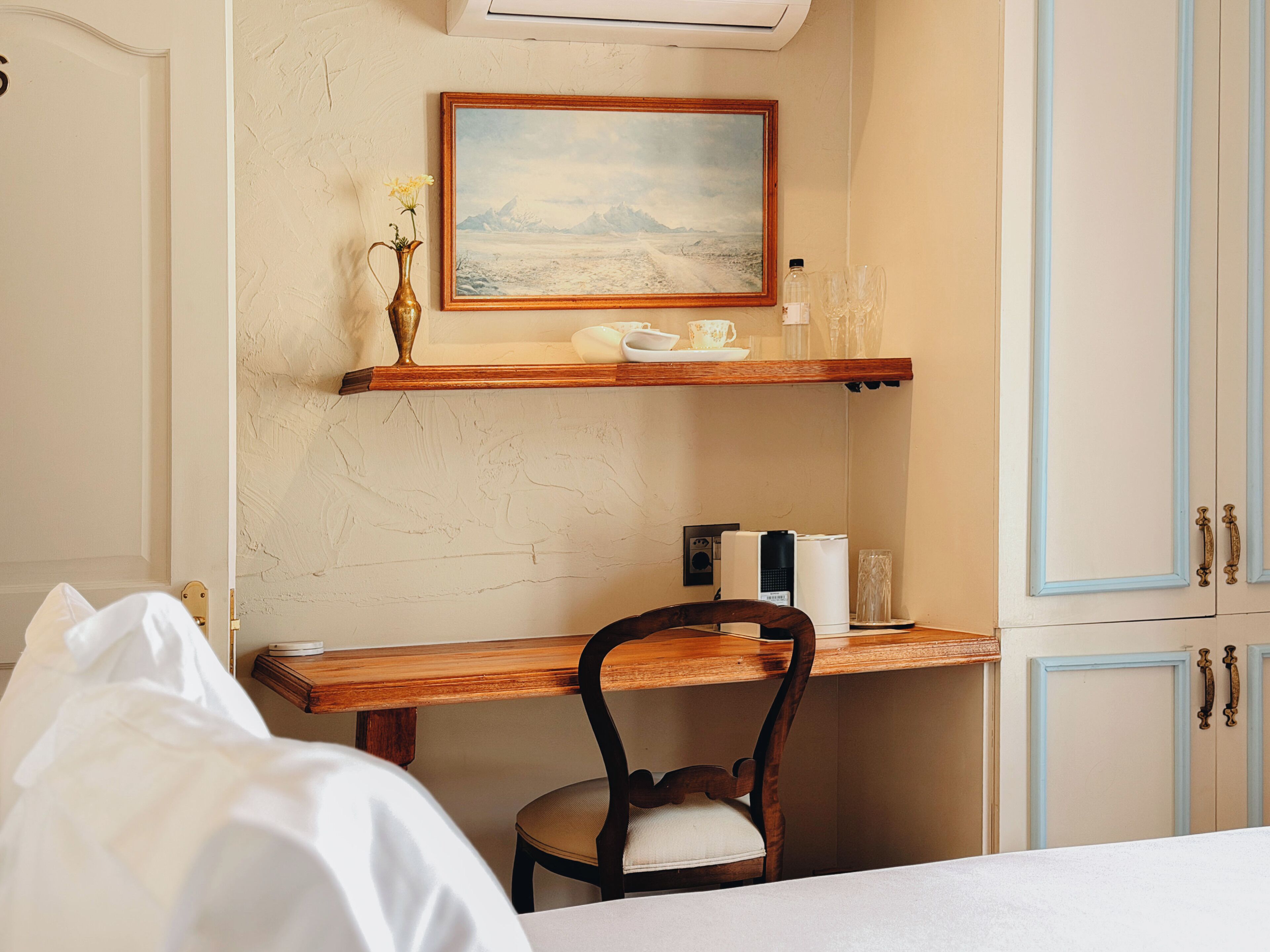 A room with a bed, a wooden desk, a chair, a painting, and a cabinet.