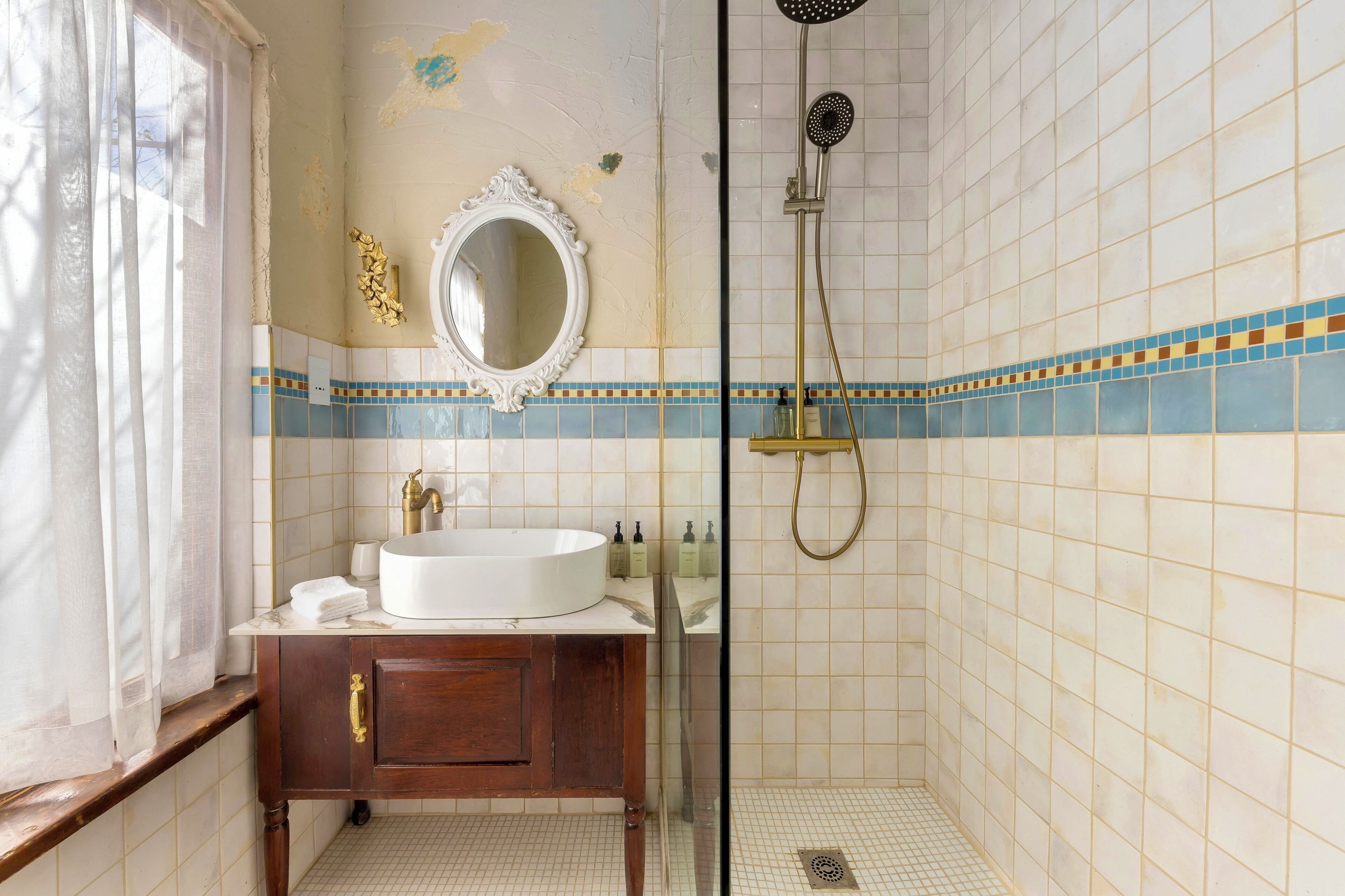 A bathroom with a white sink, wooden vanity, a mirror, and a shower.