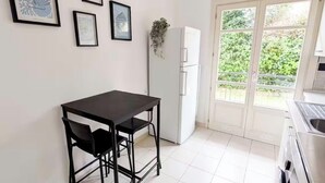 Una piccola cucina con un tavolo e sedie neri, un frigorifero bianco e una porta vetrata scorrevole che dà su un balcone.