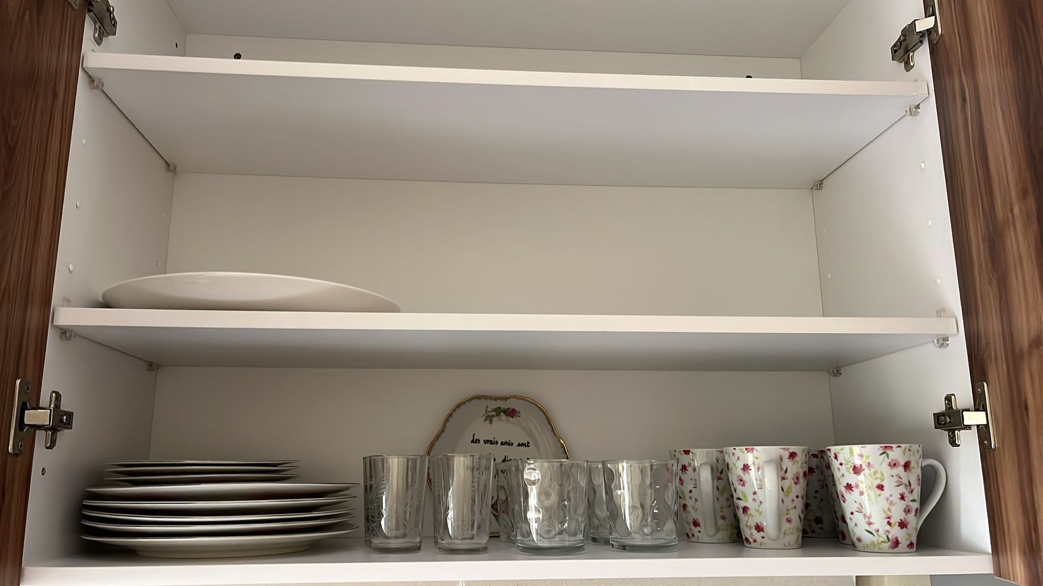 Un armario blanco con estantes, que contiene platos, vasos y tazas con motivos florales.