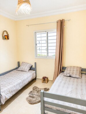 A bedroom with two single beds, a window with curtains, a small stool, and a rug on the floor. - Marrakech Airport Highlights - 5 min (Marrakech)