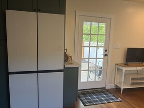 A room with a white door, a television on a wooden stand, and a small white table. - Walkable 2-bedroom Land Park Cottage (Sacramento)