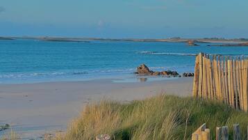 A beach with a wooden fence in the foreground, a sandy shore, and calm blue water.