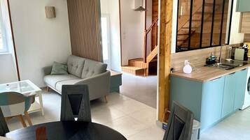 A modern living space with a sofa, dining table, kitchen area, and a staircase leading to an upper level.
