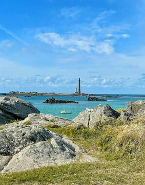 A coastal landscape with a lighthouse, rocky terrain, and a boat in the water. - Gîte Ty an Aber sur l’Aber Benoit (Saint-Pabu)