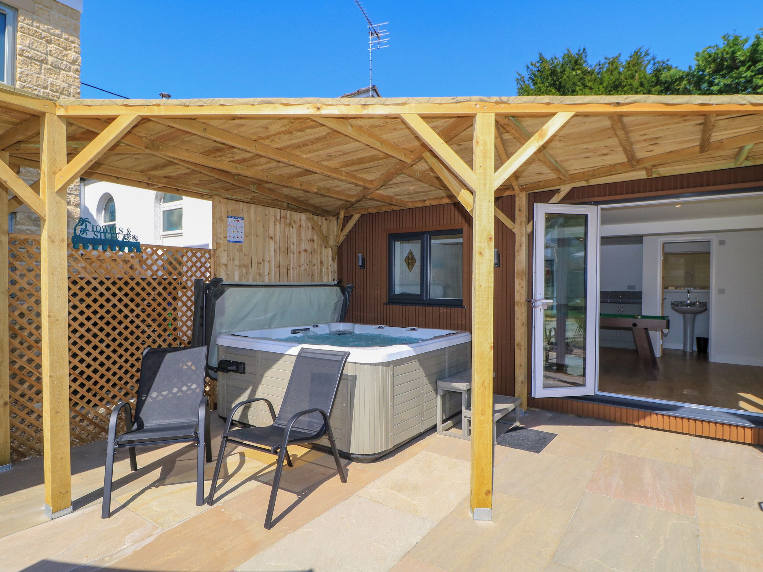 Ein überdachter Außenbereich mit Whirlpool, Stuhl und einer Holzpergola.