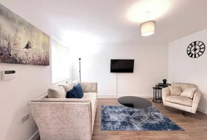 Un saló modern amb un sofà, una taula de centre, un televisor de pantalla plana fixat a la paret i un rellotge decoratiu.