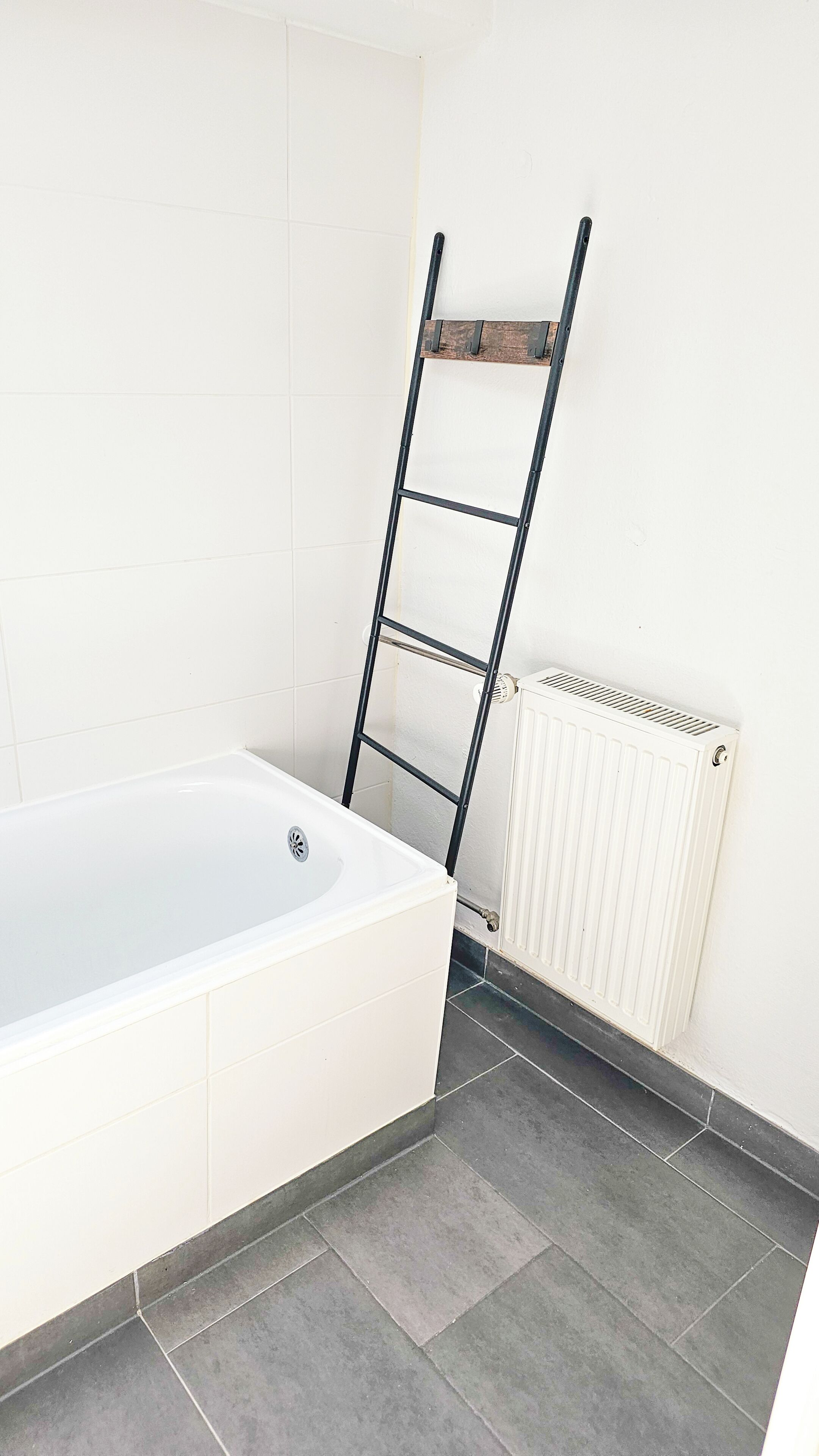 A bathroom with a white bathtub, a black metal ladder leaning against the wall, and a white radiator.