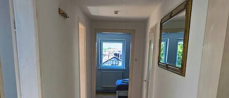 A hallway with wooden flooring, a door with a handle, and a window with a view of buildings.