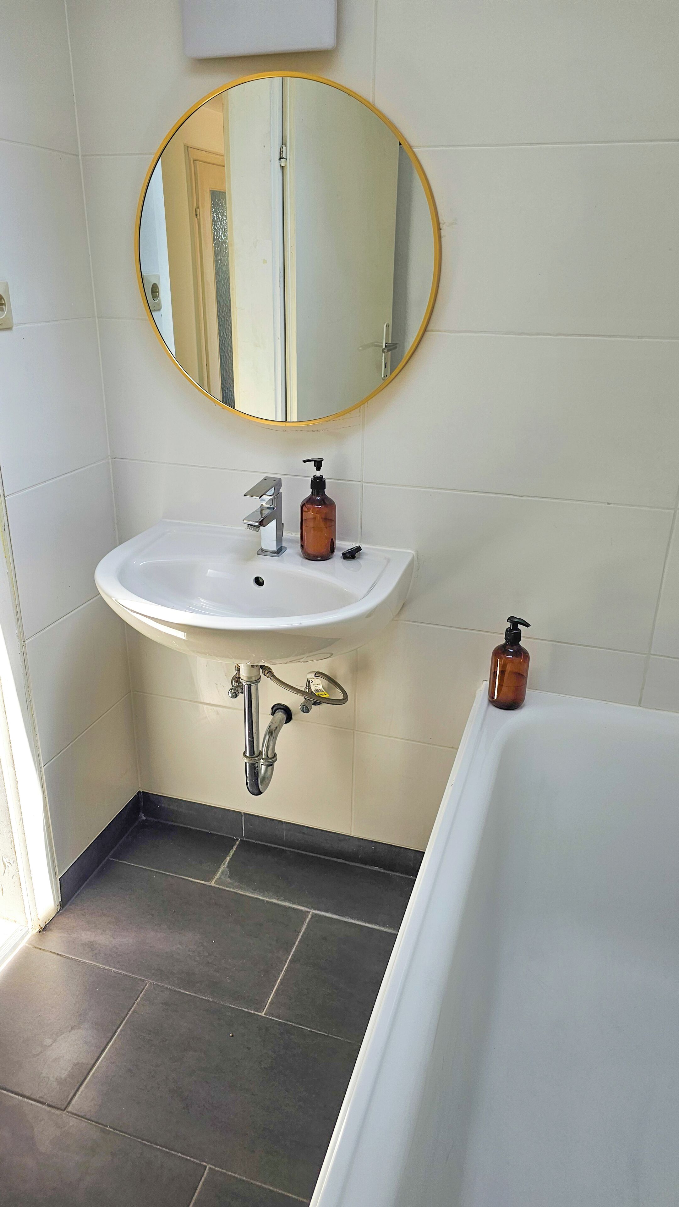 Ein Badezimmer mit einem weißen Waschbecken, einem runden Spiegel, zwei Seifenspendern und einer Badewanne.