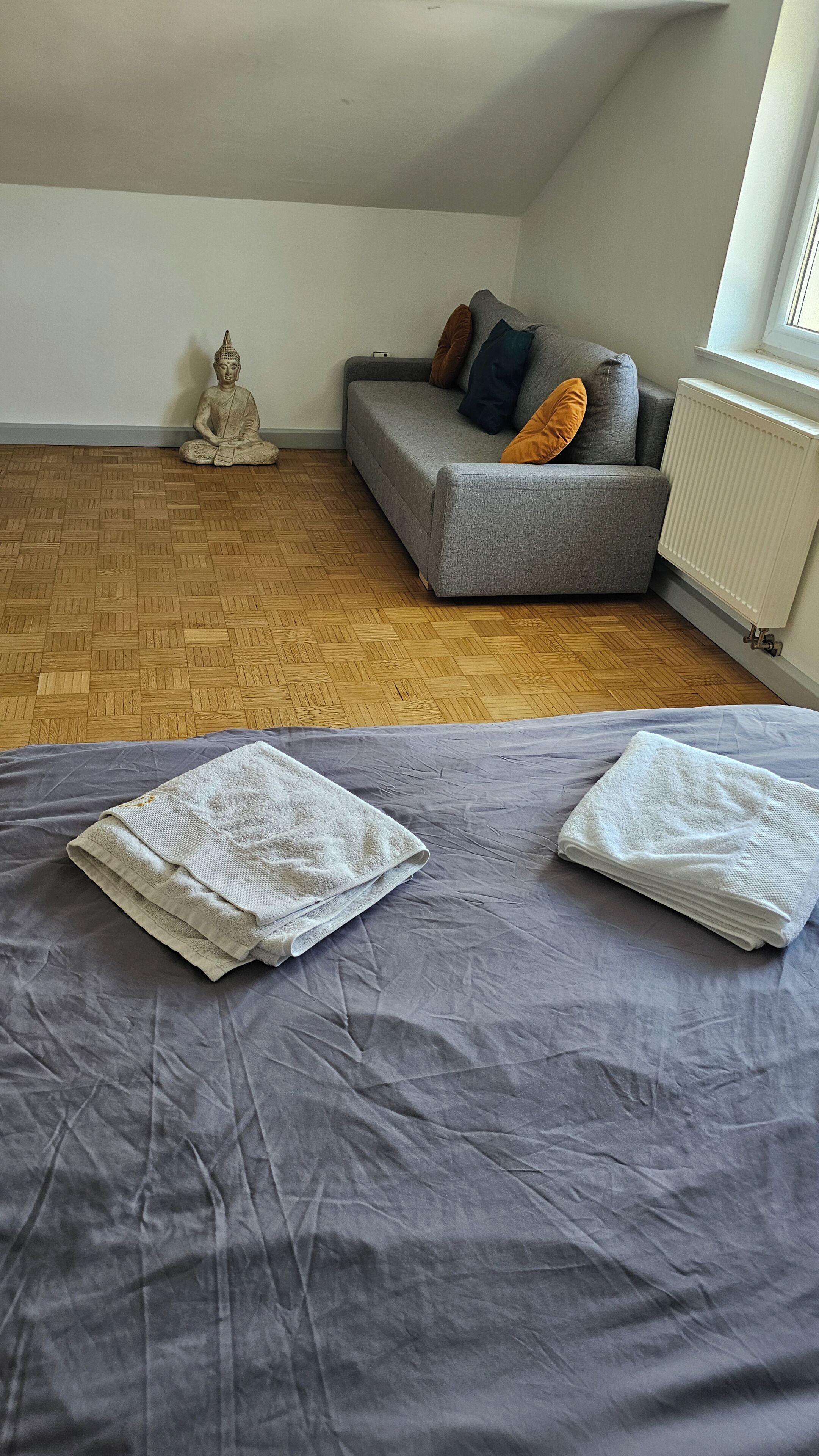 A room with a grey sofa, a meditation statue, and a radiator.