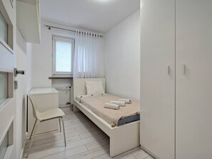A compact bedroom with a single bed, a chair, a small desk, and a window with curtains. - Gdańsk Wrzeszcz Apt — Parks Nearby & City Access (Gdańsk)