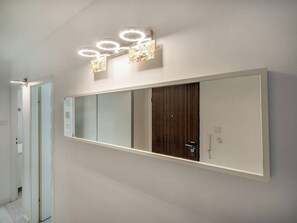 A modern bathroom with a large mirror, a wooden door, and a wall-mounted light fixture.