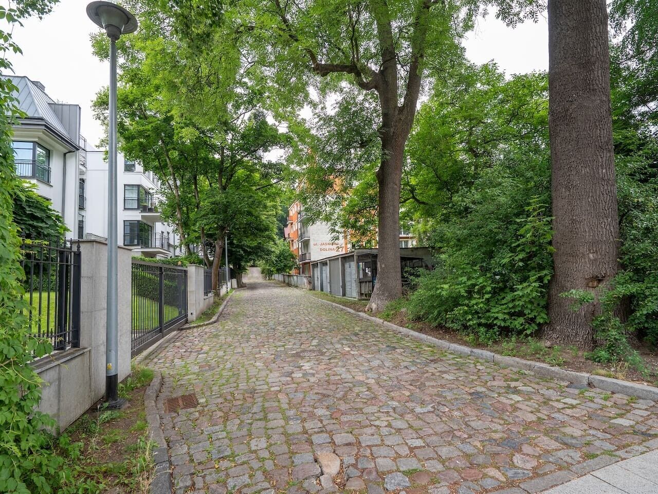 A cobblestone street lined with trees and a building with a sign that reads 'DOLINA 27'.