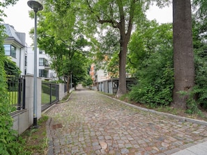 A cobblestone street lined with trees and a building with a sign that reads 'DOLINA 27'.