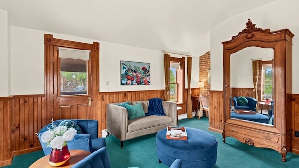 A room with wooden paneled walls, a large mirror, a sofa, a chair, and a small table with a vase of flowers.