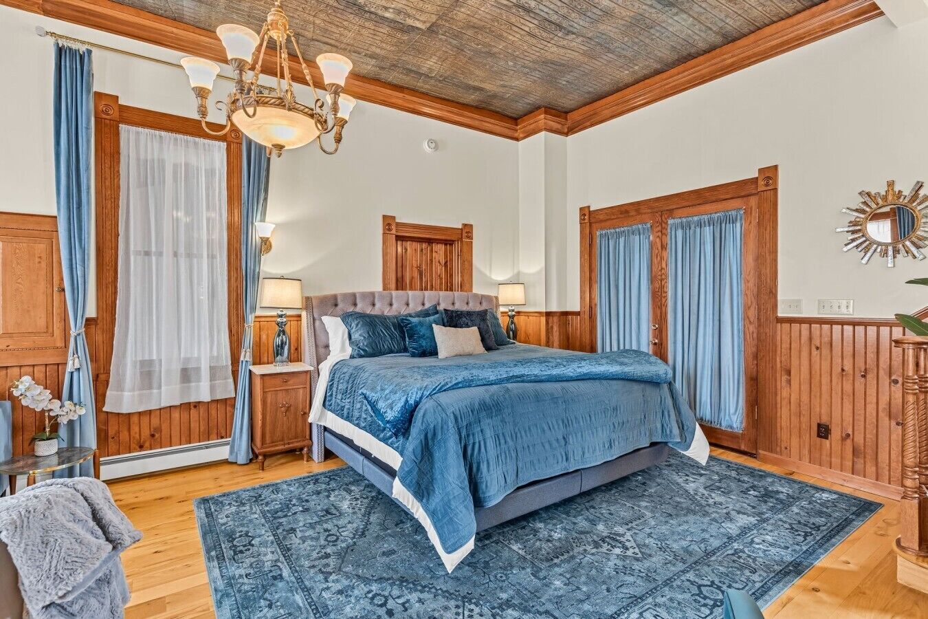 Ein Schlafzimmer mit einem großen Bett, Holzwandverkleidung, einer Kristallleuchtre und einem gemusterten Teppich.
