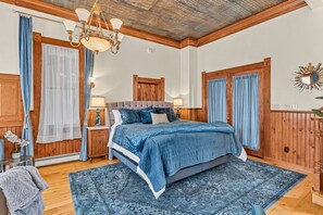 A bedroom with a large bed, wooden paneling, a chandelier, and a patterned rug.