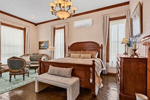 A bedroom with a wooden bed, a bench, a chair, a dresser, and a chandelier.