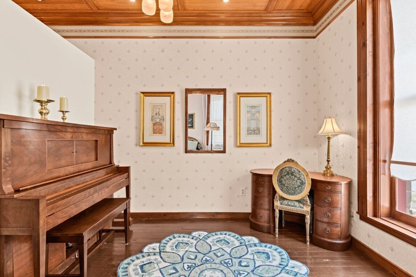 A room with a wooden piano, a patterned rug, a mirror, and a dresser with a lamp.